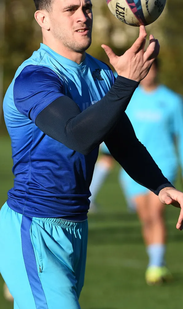 Male rugby player wearing a blue rugby shirt with a black baselayer top throwing the ball in the air