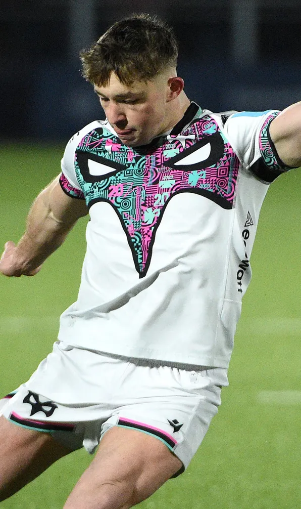Ospreys Rugby Ospreys player kicks the ball wearing the white away shirt with green and pink osprey graphic